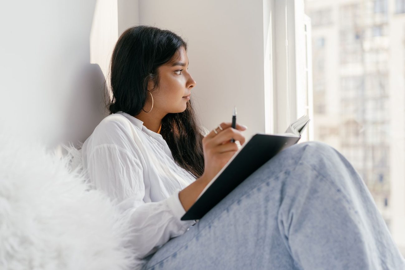 Persona escribiendo con calma junto a una ventana, en un momento de reflexión
